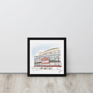 May include: Framed watercolor print of a baseball stadium with a red sign. The artwork features a black frame and is set against a white wall and wooden floor. The stadium has green and red accents.