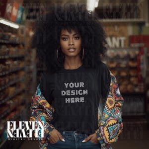 Puede incluir: Una camiseta negra con el texto "YOUR DESIGN HERE" en blanco. La persona lleva una chaqueta estampada colorida sobre la camiseta y unos vaqueros azules. Grandes pendientes de aro dorados completan el look. El fondo es un supermercado borroso.
