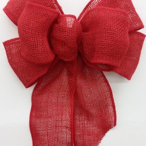 May include: A large, vibrant red burlap bow. The bow is made of a loosely woven fabric, with multiple loops and tails. The bow is a festive decoration, perfect for adding a touch of color to any occasion.