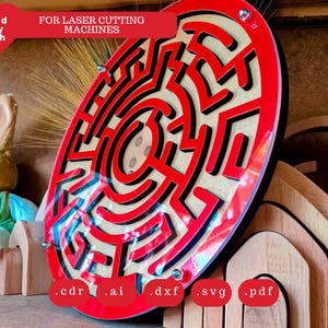 May include: A red and black laser-cut wooden maze with the text "FOR LASER CUTTING MACHINES". The maze is oval-shaped and has a complex design. A stuffed bunny and wooden shapes are in the background.