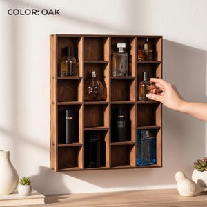 Può includere: Una mensola da parete quadrata in legno color rovere con sedici scomparti individuali. L'organizzatore a griglia contiene vari flaconi di profumo in vetro di diverse forme e dimensioni. Il testo COLOR: OAK è visibile in alto a sinistra.