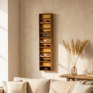 Peut inclure: Un organisateur de lunettes de soleil en bois, de forme rectangulaire et fixé au mur. Il comporte plusieurs étagères, chacune contenant une paire de lunettes de soleil de différents styles et couleurs. Le bois est de couleur chaude et naturelle.