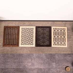 Op de afbeelding: Vier rechthoekige houten decoratieve panelen met ingewikkelde uitgesneden ontwerpen. De panelen hebben patronen van bladeren, geometrische vormen en golfachtige vormen. De panelen zijn in tinten bruin, crème en donkerbruin, gerangschikt op een grijze ondergrond.