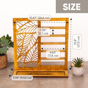 May include: A wooden jewelry display stand with a laser-cut leaf pattern on the left and multiple rows of earring slots on the right. The base features the name Amanda. Dimensions are 10.47 inches wide, 10.8 inches high, and 3.76 inches deep.