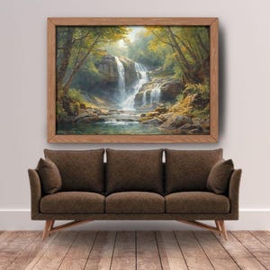 May include: A framed landscape painting depicts a waterfall cascading into a pool, surrounded by lush greenery. The artwork hangs above a brown sofa with three cushions and wooden legs, set against a white wall and hardwood floor.