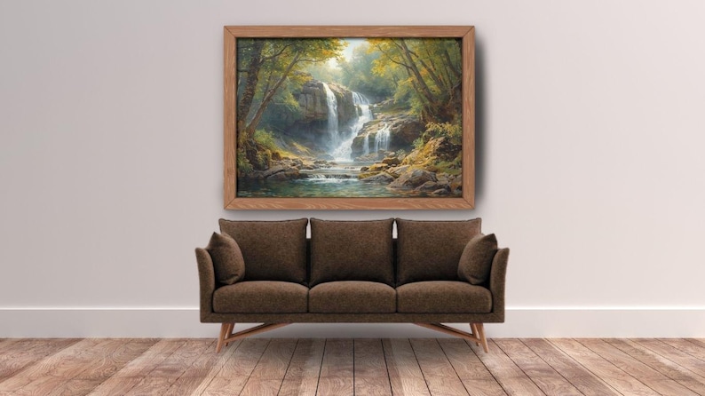 May include: A framed landscape painting depicts a waterfall cascading into a pool, surrounded by lush greenery. The artwork hangs above a brown sofa with three cushions and wooden legs, set against a white wall and hardwood floor.