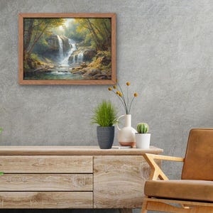 May include: A framed landscape painting of a waterfall in a forest hangs on a gray wall. A wooden cabinet with plants and a leather chair are in front of the wall. The painting has a brown frame.