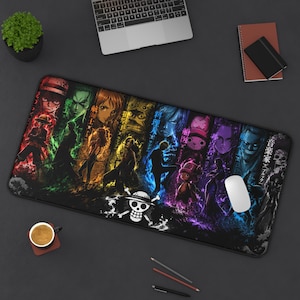 Pode incluir: Um tapete de secretária retangular com uma ilustração vibrante e multicolorida de várias personagens de anime de One Piece. O design inclui um logótipo central de caveira e ossos cruzados com um chapéu de palha num fundo escuro.