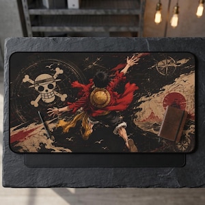 Puede incluir: Una alfombrilla de escritorio rectangular con una ilustración de anime de One Piece de Monkey D. Luffy alcanzando hacia arriba. El diseño incluye un emblema de calavera, una rosa de los vientos y un sol rojo sobre un mapa oscuro con un cuaderno marrón.