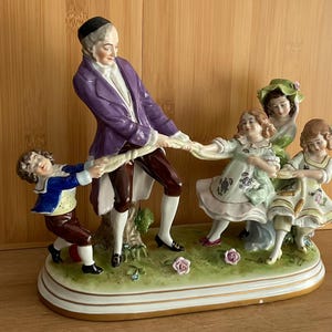 Figura de porcelana de Scheibe-Alsbach, Alemania, siglo XX: Hombre y niños jugando a la soga.