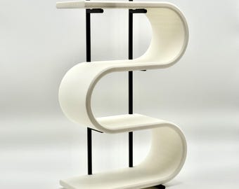 May include: A modern, white, three-tiered shelf unit with a unique, flowing design. The shelves are supported by black metal vertical posts. The unit has a distinctive, curved shape, and the shelves are rectangular. The overall aesthetic is minimalist and contemporary.