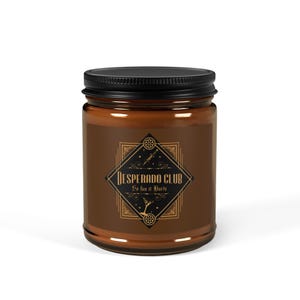 Op de afbeelding: Bruine glazen potkaars met een zwart deksel. Het etiket bevat de woorden "Desperado Club" in een decoratief lettertype, samen met de zin "So fun it Hurts". Het etiket heeft een goud- en zwart art-deco ontwerp.