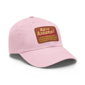 Könnte beinhalten: Hellrosa Baseballkappe mit gebogenem Schirm. Auf der Kappe befindet sich ein brauner Aufnäher mit den Worten "NEE EELM ACHIEVEMENT!" in einer stilisierten Schriftart. Darunter steht der Text "YOUR PERSONALIZED ACHIEVEMENT HERE! ADD A REWARD IF YOU WANT."
