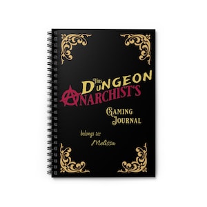 May include: Black spiral-bound notebook with the text "This Dungeon Anarchist's Gaming Journal" in gold and red. The notebook has gold decorative corner designs and the name "Melissa" below the title.