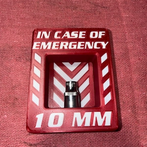 May include: Red 3D-printed case with the text "IN CASE OF EMERGENCY" and "10 MM" in white. Inside the case is a silver socket. The case has white diagonal stripes on the sides.