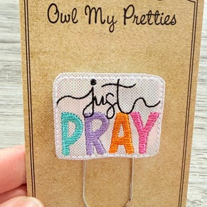 May include: Embroidered bookmark with the words "just PRAY" in colorful letters. The bookmark is attached to a brown card with the text "Owl My Pretties" and a website address. The bookmark has a silver metal clip.