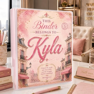 May include: A light pink binder featuring a Parisian-style building illustration, the text "THIS Binder BELONGS TO Kyla", and a "Proverbs 16:3" scripture verse. The cover has gold accents, a postmark stamp, and a soft, watercolour-inspired aesthetic.