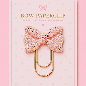 May include: A pink bow paperclip with a gold-coloured clip. The bow is covered in iridescent rhinestones and is attached to a gold-coloured paperclip. The card reads "BOW PAPERCLIP" in gold lettering.