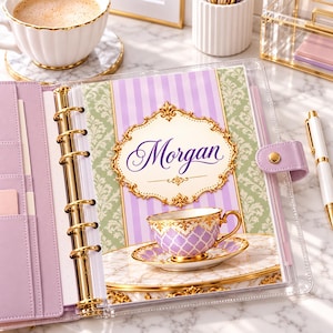 Può includere: Un'agenda personale con copertina trasparente e anelli dorati, dotata di un inserto con motivo damascato color lavanda e verde. La pagina di copertina mostra il nome Morgan in corsivo viola all'interno di una cornice dorata decorata.