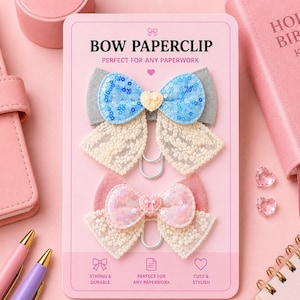 May include: Two bow-shaped paperclips on a pink card. The top bow is blue with sequins and a yellow heart, the bottom is pink. The card reads "BOW PAPERCLIP" and "PERFECT FOR ANY PAPERWORK".