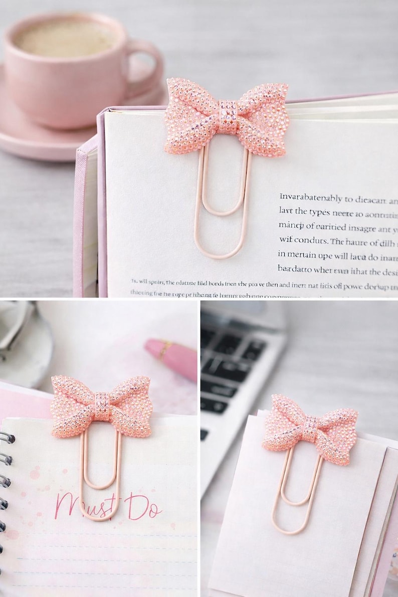 May include: Glittery pink bow-shaped paper clips. The clips are attached to pages of a notebook and a book. The words "Must Do" are written on one of the pages. A pink cup and saucer are in the background.