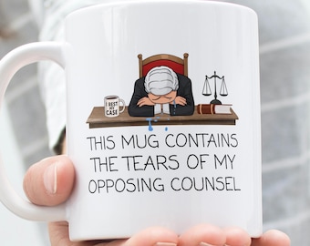 May include: White ceramic mug with a humorous design. The mug features an illustration of a slumped-over judge and the text: "THIS MUG CONTAINS THE TEARS OF MY OPPOSING COUNSEL."