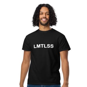 Puede incluir: Una camiseta negra con la palabra "LMTLSS" impresa en blanco. La persona lleva vaqueros azules y zapatillas blancas. La persona sonríe y mira a la cámara.