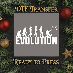 May include: A gray DTF transfer design with the word "EVOLUTION" in white, depicting the evolution of humans. The design includes the text "DTF TRANSFER" and "READY TO PRESS" in gold. The image is decorated with Christmas ornaments and pine branches.