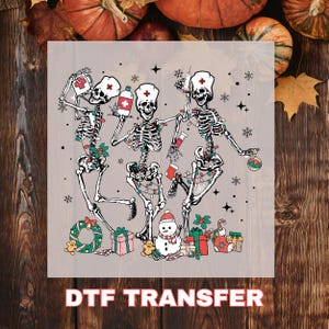 May include: A DTF transfer featuring three skeleton figures dressed as nurses, holding medical supplies and Christmas ornaments. The design includes a snowman, presents, and the text "DTF TRANSFER".
