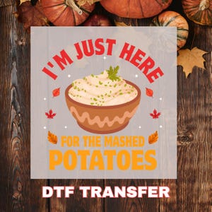 May include: A DTF transfer with a graphic of mashed potatoes in a brown bowl. The text reads "I'M JUST HERE FOR THE MASHED POTATOES". Autumn leaves and pumpkins are in the background.