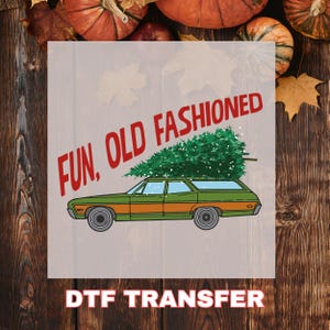 May include: A graphic featuring a green and orange station wagon with a Christmas tree on top. The words "FUN, OLD FASHIONED" are in red, and "DTF TRANSFER" is at the bottom. The background is a wood grain pattern.