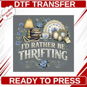 May include: A DTF transfer design featuring the text I'D RATHER BE THRIFTING in white and blue. The illustration includes a yellow lamp, stacked books, a string of pearls, a blue and white teacup, a decorative plate, and two frames with a price tag.