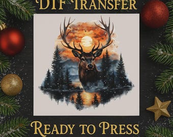 Op de afbeelding: DTF-transfer met een aquarel schilderij van een hert met groot gewei, tegen een zonsondergang boven een bos en meer. De tekst "DTF TRANSFER" en "READY TO PRESS" staat in gouden letters.