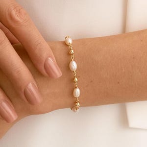 May include: A delicate gold chain bracelet featuring alternating small white oval pearls and tiny gold beads. The bracelet is designed with a simple link structure, showcasing a refined combination of lustrous pearl accents and metallic gold elements.