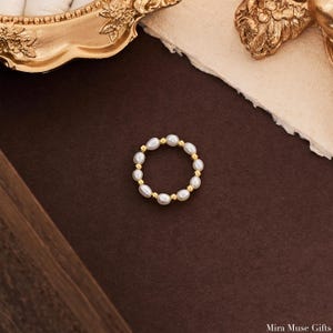 May include: A circular ring featuring alternating white oval-shaped pearls and small metallic gold-toned beads. The jewelry piece is arranged in a continuous loop, showcasing a repeating pattern of individual pearls separated by single gold-colored beads.