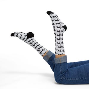May include: White socks with a black dachshund pattern. The socks have black heels and toes. The person is wearing blue jeans.