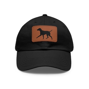 May include: Black baseball cap with a brown leather patch featuring a silhouette of a dog. The cap has a curved brim and a classic six-panel design. The dog silhouette is in a running pose.