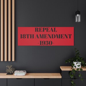 May include: A red rectangular canvas with the words "REPEAL 18TH AMENDMENT -1930-" in black. The canvas is mounted on a dark gray wall above a wooden cabinet. A decorative plant and a hanging light are also visible.