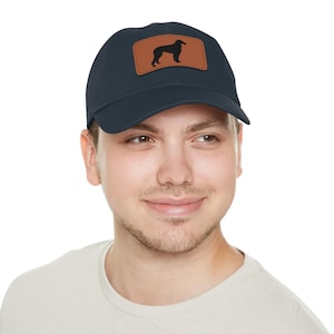 May include: Navy blue baseball cap with a brown leather patch featuring a black silhouette of a dog. The cap is made of a soft material and has a curved brim. A stylish accessory for dog lovers.