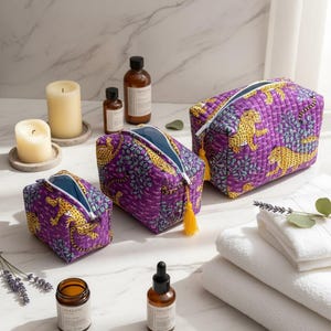 Könnte beinhalten: Drei gesteppte Kosmetiktaschen mit lila Hintergrund und gelbem Leopardenmuster. Die Taschen haben ein blaues Innenfutter und eine gelbe Quaste am Reißverschluss. Die Taschen werden mit Kerzen, ätherischen Ölen und weißen Handtüchern präsentiert.