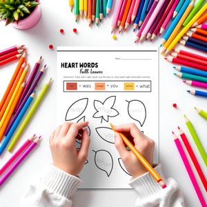 May include: A worksheet titled "HEART WORDS Fall Leaves" with leaf outlines and sight words. A person is using a yellow pencil to trace the words. Colorful pencils surround the worksheet on a white surface.