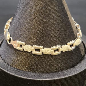 May include: A silver-toned link bracelet featuring alternating rectangular segments with a textured, matte finish and smooth, polished connecting loops. The bracelet includes a secure lobster claw clasp mechanism for fastening around the wrist.