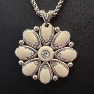 Puede incluir: Collar con colgante de flor plateado. El colgante presenta un dise&ntilde;o de flor esmaltada color crema con detalles de cristal. El collar tiene una cadena trenzada y un cierre de mosquet&oacute;n.