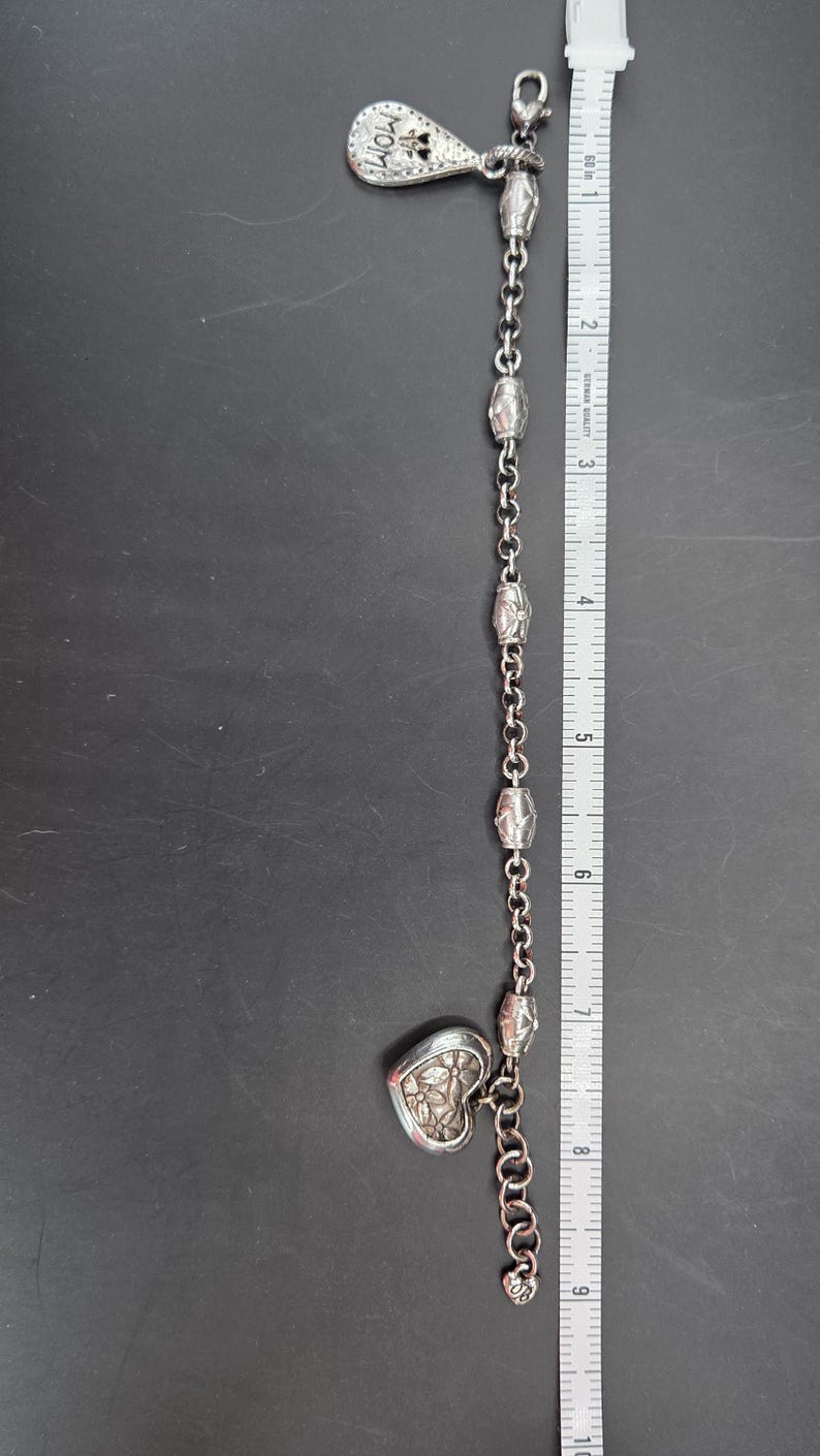 May include: Silver-toned bracelet with a teardrop-shaped charm that reads "MOM" and a heart-shaped charm. The bracelet is approximately 9 inches long and features a chain with decorative links. A ruler is next to the bracelet.