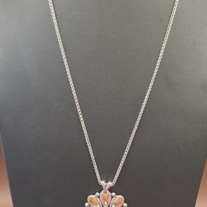 Puede incluir: Collar plateado con un colgante de flor. El colgante presenta una piedra central transparente rodeada de elementos en forma de p&eacute;talo en oro y plata. La cadena es de dise&ntilde;o delicado y tejido.
