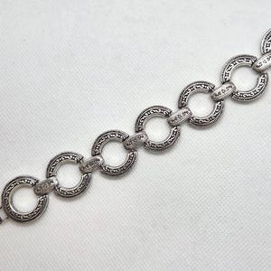 May include: Silver-toned bracelet featuring a series of interconnected, circular links. Each link is adorned with an intricate, embossed pattern and connected by smaller, decorative elements. The bracelet has a clasp closure.
