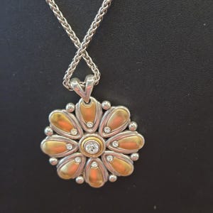 Puede incluir: Collar plateado con colgante de flor. El colgante presenta p&eacute;talos dorados, peque&ntilde;as piedras preciosas transparentes y una piedra preciosa central transparente. La cadena es de dise&ntilde;o tejido.