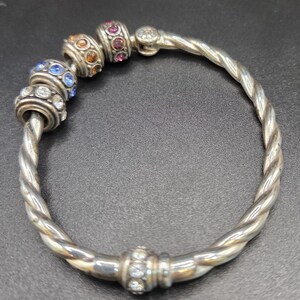 Puede incluir: Pulsera plateada con dise&ntilde;o retorcido. La pulsera presenta cuentas decorativas con piedras preciosas de colores azul, naranja y rosa. Es una pieza de joyer&iacute;a.