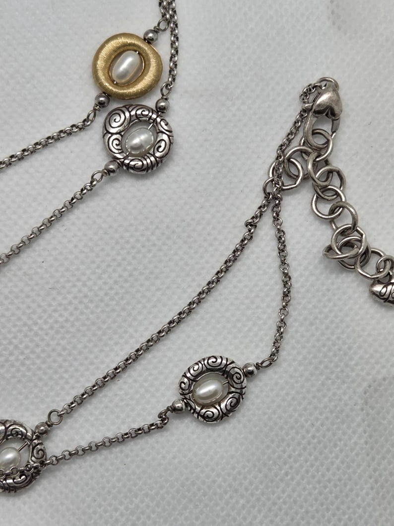 May include: Silver necklace with multiple strands and decorative elements. The necklace features a gold-toned pendant with a pearl, and other pendants with pearls set in ornate silver frames. The chain has a lobster clasp.