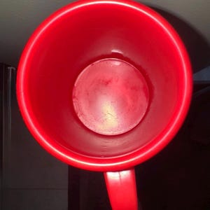 以下が含まれることがあります： 上から見た、持ち手付きの鮮やかな赤いマグカップ。マグカップの内側には円形の底が見えます。マグカップは、しっかりとした不透明な素材で作られています。